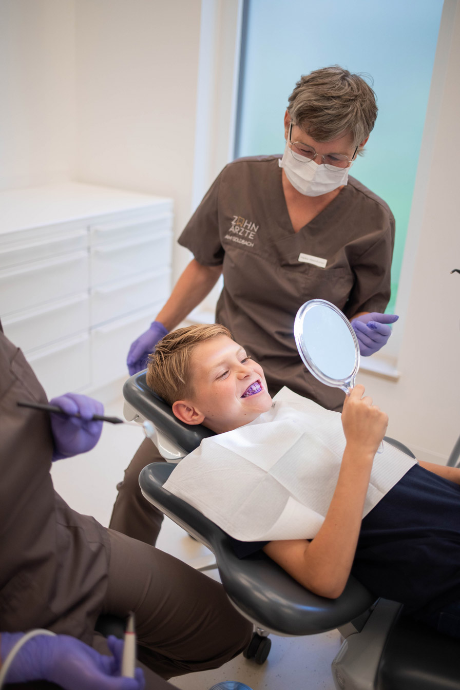 Zahnärzte am Goldbach, Kind im Behandlungszimmer, lacht mit eingefärbten Zähnen.